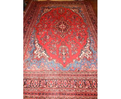 A large red ground Mashad carpet, decorated with floral tear drop medallion to centre, within foliate borders, fringed, L.370