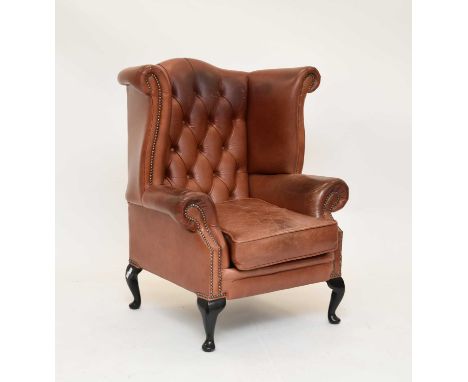 A reproduction tan leather button-back wing armchair, on mahogany cabriole supports, 92cm wide x 69cm deep x 106cm high, seat