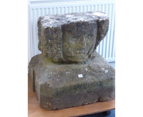 An early carved stone head raised upon a large rectangular stone plinth base with canted corners and angular top, the face al