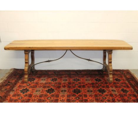 Spanish elm dining table with substantial plank top, raised on carved shaped H-form trestle supports united by scrolled metal