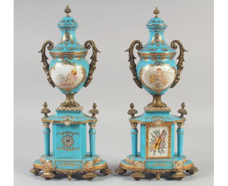 A PAIR OF SEVRES STYLE LIGHT BLUE PORCELAIN AND ORMOLU TWO HANDLED URNS AND COVERS on stands, edged in gilt with panels of mu