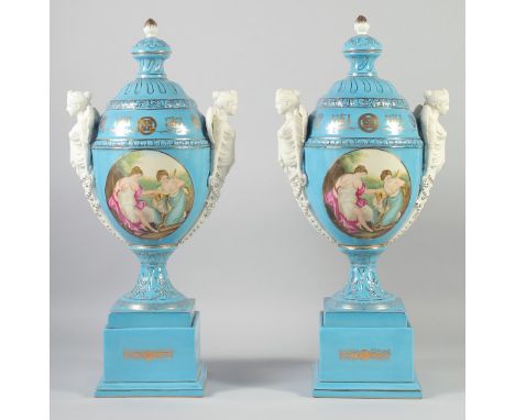 A LARGE PAIR OF CONTINENTAL LIGHT BLUE TWO HANDLED URNS AND COVERS with classical female heads, on stands. 21ins high.