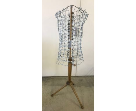 A vintage adjustable dress makers dummy. Metal frame work on a wooden tripod stand. Shortest position 136 cm tall.