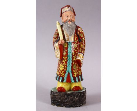 A 19TH / 20TH CENTURY CHINESE FAMILLE ROSE PORCELAIN FIGURE OF AN IMMORTAL, stood upon a wood style base holding a scroll, 22