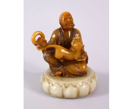 A CHINESE CARVED AMBER COLOUR SOAPSTONE FIGURE OF LOUHAN - in a seated pose with a kyllin and a bangle in his hand, his ronbe