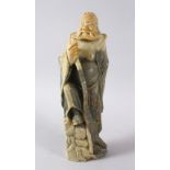 A LARGE CHINESE SOAPSTONE CARVING OF AN IMMORTAL, stood upon a rocky outcrop with a double groud,