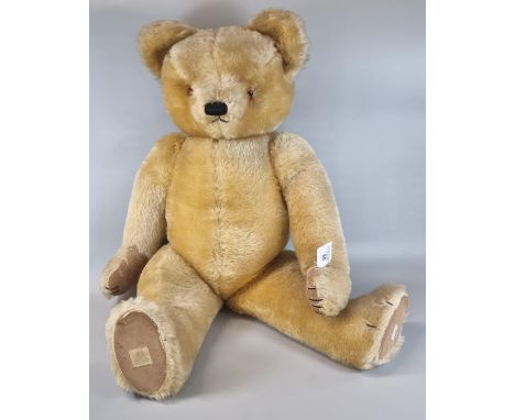 20th century growler teddy bear with stitched nose, moveable limbs and padded hands and feet.  The stitched label to one foot