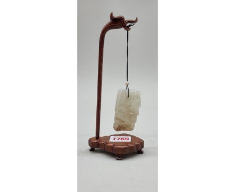 A Chinese carved and pierced celadon jade pendant, in the form of a stylized qilin, 6.2 x 4cm, on carved hardwood stand. 