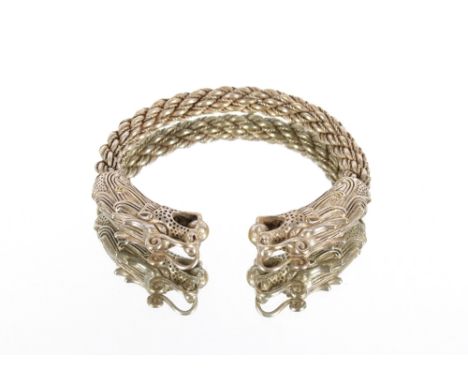 A Tibetan white metal bangle of twist design, with dragon head terminals