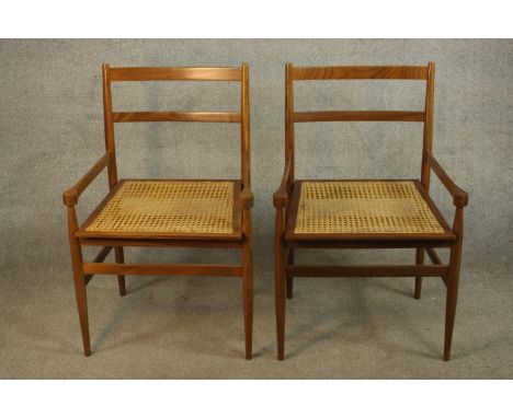 A pair of mid 20th century beech framed ladder back carver dining chairs with cane seats, raised on tapering supports and tur