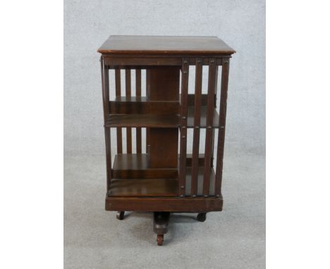 An early 20th century oak three shelf rotating book stand raised on metal cross shaped stretcher terminating on casters. H.83