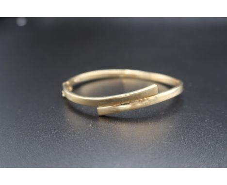 A 9ct gold crossover style bangle. Weight 7.03 grams.