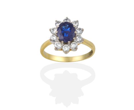 the oval cut sapphire within a border of round brilliant cut diamonds, in white claw settings, to a yellow tapered shoulder p