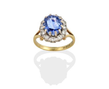 the oval cut sapphire within a border of round brilliant cut diamonds, in white claw settings, to a yellow forked shoulder pl