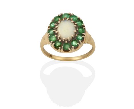 the oval cabochon opal within a border of round cut emeralds, in yellow claw settings, to a tapered shoulder plain polished s