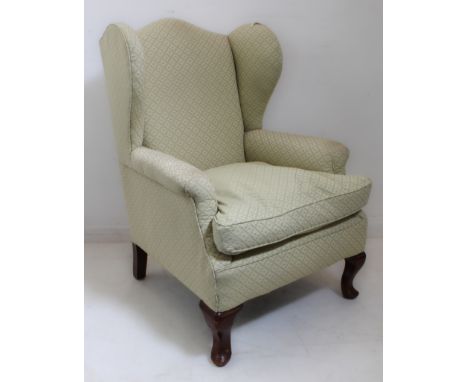 An early 20th century wing-backed armchair in early 18th century style; light lime-green upholstery and raised on short cabri