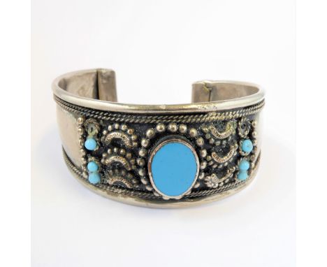 A continental silver (unmarked) bangle: centrally set with an oval turquoise flanked by na&iuml;ve style decoration in relief