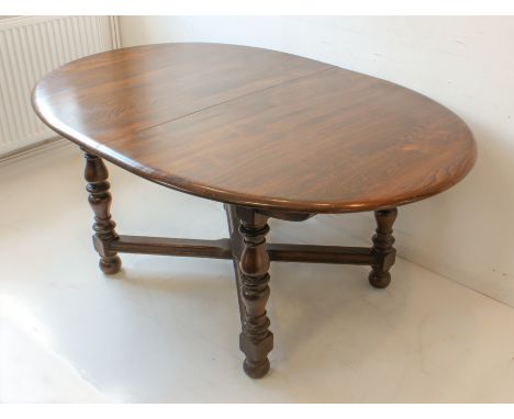 An Ercol extending oval-topped elm dining table on four turned supports united by a cross frame stretcher (164cm without leaf