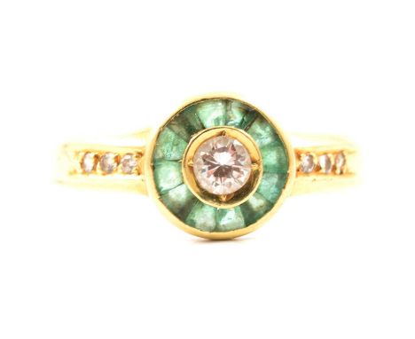 An emerald and diamond cluster ring, a central brilliant cut diamond claw set in a round collet and surrounded by twelve tape