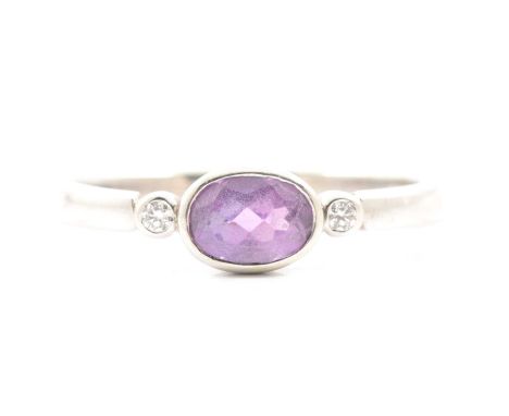 An amethyst and diamond three stone ring, the 7x5mm oval mixed cut amethyst collet set horizontally with a small brilliant cu