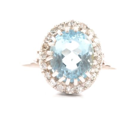 An aquamarine and diamond cluster ring, the oval mixed cut aquamarine 10x8mm, claw set and surrounded by twenty 8 and brillia