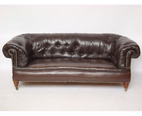 A late Victorian Chesterfield sofa, buttonback upholstered in brass tacked dark brown leather, raised on turned forelegs and 