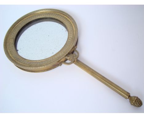 A 19th Century French Empire style gilt bronze hand mirror, the circular mirror within a surround with a stiff leaf band, on 