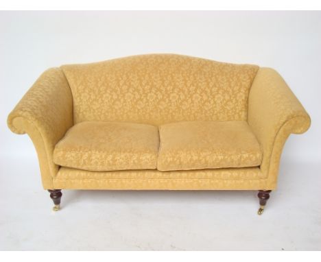 A modern two seater sofa, with humpback, scroll arms and two squab cushions, on turned forelegs and brass casters, upholstere