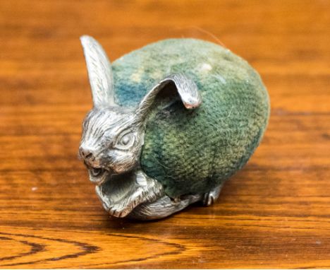 A silver pin cushion stamped silver underside with green velvet 'cushion' modelled as a laughing Hare, late 19th/early 20th C
