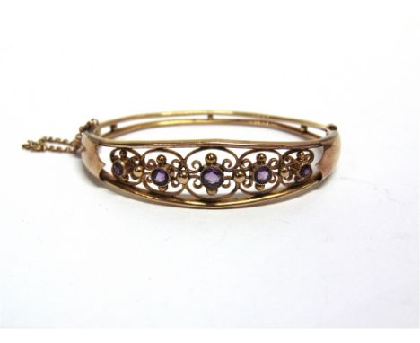 AN EDWARDIAN FIVE STONE AMETHYST HINGED BANGLE  the graduated amethysts in wirework settings, tagged '9ct', internal diameter