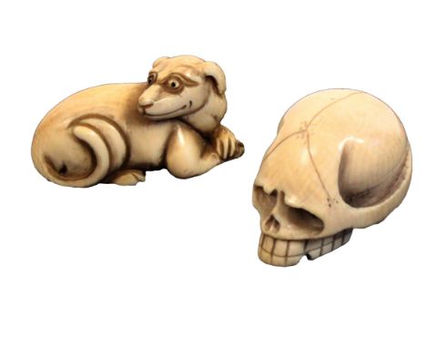 Two early 20th Century ivory netsuke, comprising a skull, 4cm, and a hound at rest, 4.5cms. &nbsp; &nbsp; (2)&nbsp; &nbsp; &n