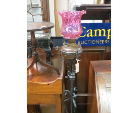 A wrought iron floor lamp, with copper oil reservoir and pink glass shade 