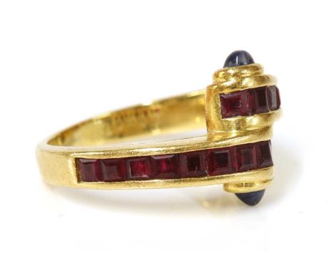 A gold ruby and sapphire crossover ring,the crossover head channel set with square step cut rubies, with an oval cabochon sap