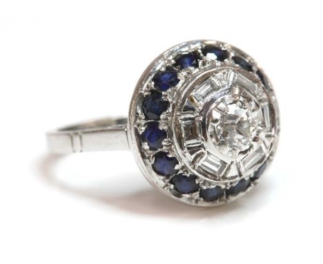 A white gold diamond and sapphire circular stepped cluster ring,with an old European cut diamond, double claw set to a scallo