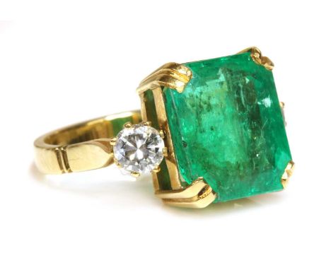 An emerald and diamond three stone ring,with an emerald cut emerald, double claw set to a plain yellow collet with pierced ho