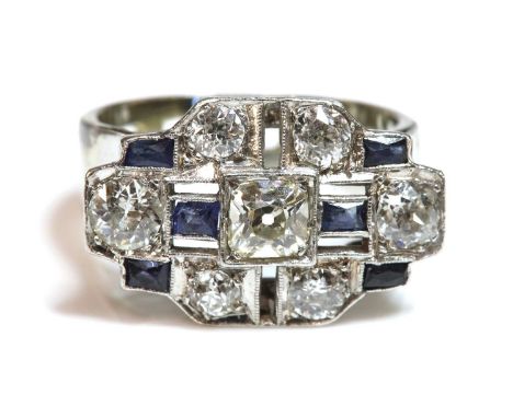 An Art Deco diamond and sapphire stepped plaque ring, c.1935,with a cushion cut diamond, grain set to a central box collet, w