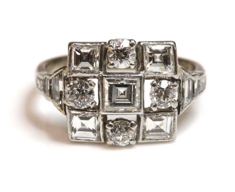 An Art Deco diamond set square cluster ring,with stepped diamond set shoulders. A square step cut diamond, rub set to the cen