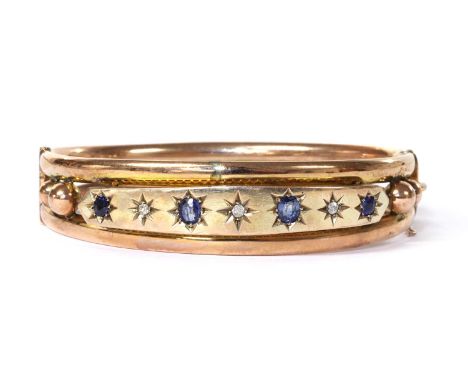 An Edwardian diamond and sapphire hinged bangle, c.1920,with a flat graduated panel to the top half. A row of graduated oval 