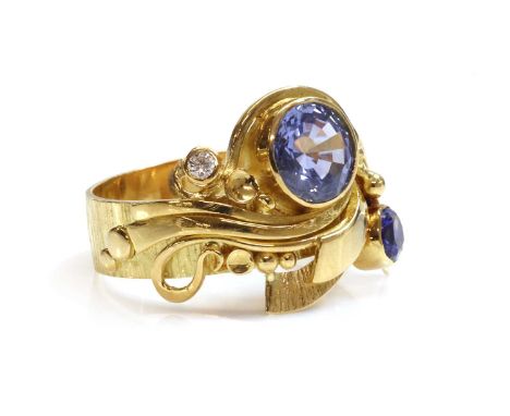 An 18ct gold sapphire and diamond ring,with a scrolling layered head. A circular mixed cut sapphire, rub set to one side, wit