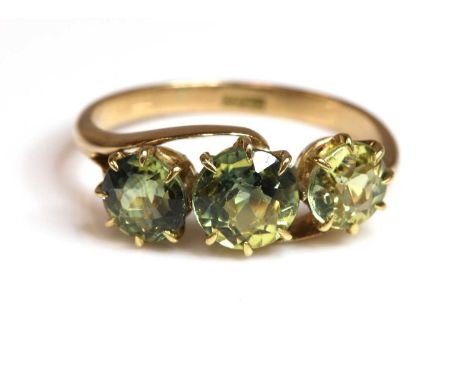 An Edwardian three stone sapphire ring,with three circular mixed cut yellow and yellow/green sapphires, claw set to shallow c