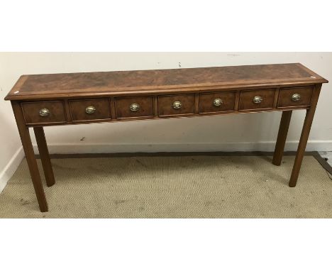 A burr walnut side table, the feathered and cross-banded top with moulded edge, over seven short drawers with pressed brass h