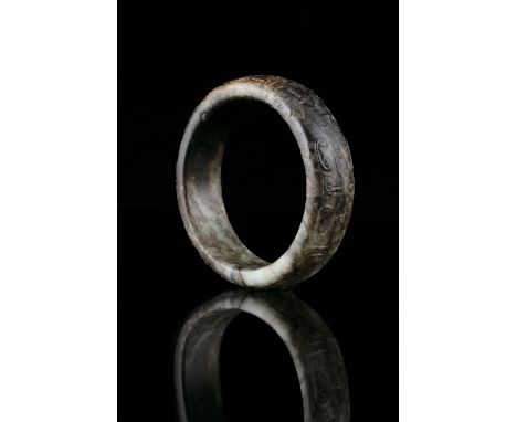 A CARVED MOTTLED JADE ARCHAISTIC BANGLE China, Antiquer, Possibly Ming Dynasty Carved in low-relief with three archaistic ins