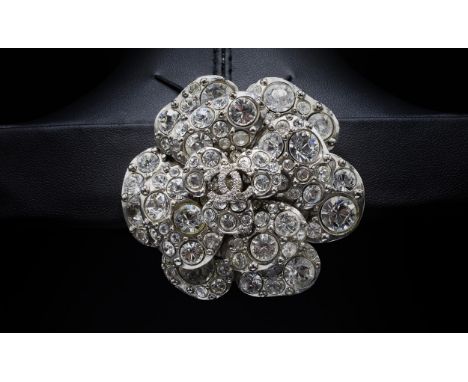 CHANEL BROOCH, iconic camellia flower with a central double CC logo, rhinestones and silver tone metal, with safety pin closu