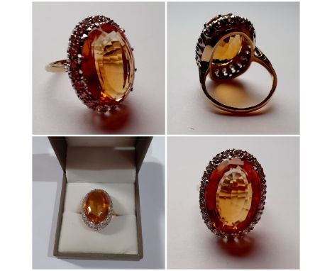 A yellow metal ring having a large faceted oval citrine cabochon to the mount measuring 2cm surrounded by a band of diamonds.