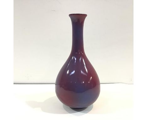 A Chinese porcelain vase in a sang-de-boeuf glaze, of flask form, mottled in red and lavender, unmarked, on a wooden stand. V