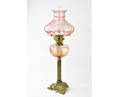 A decorative 20th century oil lamp with cranberry tinted shade and glass reservoir on a cast brass triangular shaped base, he