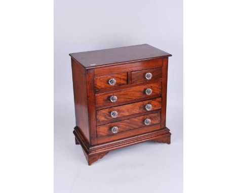 An early 20th century mahogany minature chest of two over three drawers, with glass handles and on bracket feet. 43cm high