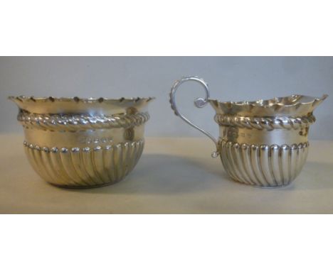 A late Victorian silver circular cream jug with demi-reeded ornament, a flared, crimped rim and an S-scrolled handle and a ma