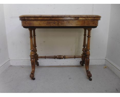 A late Victorian carved walnut and marquetry card table, the baise lined, rotating, foldover top having round corners, over a