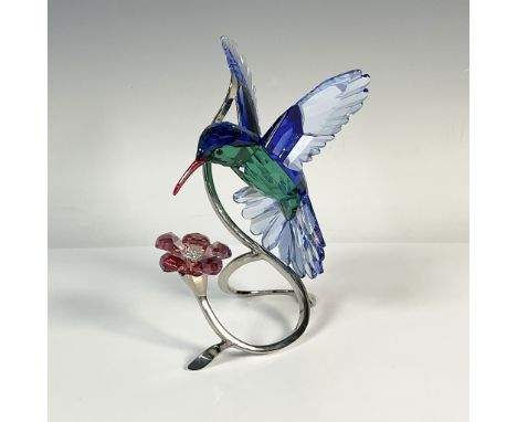 A hummingbird in flight, showcasing vibrant blue and teal coloration, is gracefully mounted on a silver tone metal display fe